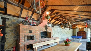 Un área de estar al aire libre de estilo rústico, con una chimenea de ladrillo, bancos de madera y una mesa.