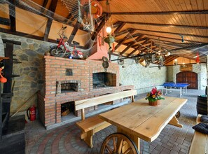 Ein rustikaler Sitzbereich im Freien mit Kamin aus Backsteinen, Holzbanken und einem Tisch.