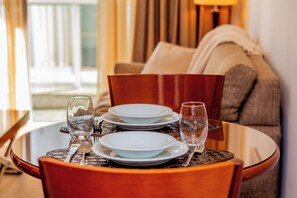 A dining table with plates, glasses, and cutlery, set against a backdrop of a sofa and curtains. - George V Flat - Itaim Bibi (São Paulo)