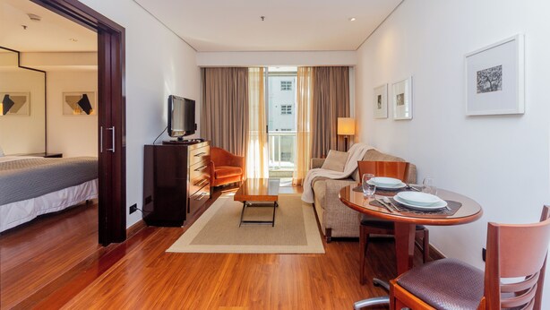 Habitación de hotel con cama, televisión, sofá, mesa de comedor con sillas y vista al exterior.