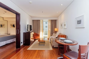 A hotel room with a bed, a TV, a sofa, a dining table with chairs, and a view of the outside. - George V Flat - Itaim Bibi (São Paulo)