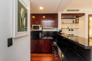 A modern kitchen with wooden cabinets, a microwave, and a gas stove. - George V Flat - Itaim Bibi (São Paulo)