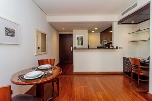 A dining area with a wooden table set for two, a kitchen with modern appliances, and a hallway leading to another room. - George V Flat - Itaim Bibi (São Paulo)
