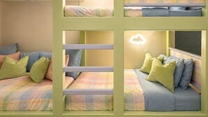 Une chambre avec des lits superposés, décorée dans des tons de vert clair, dotée d’un luminaire en forme de nuage et d’une fenêtre avec des stores.