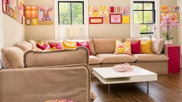 A living room with a beige sofa, a white coffee table, and a patterned ottoman.