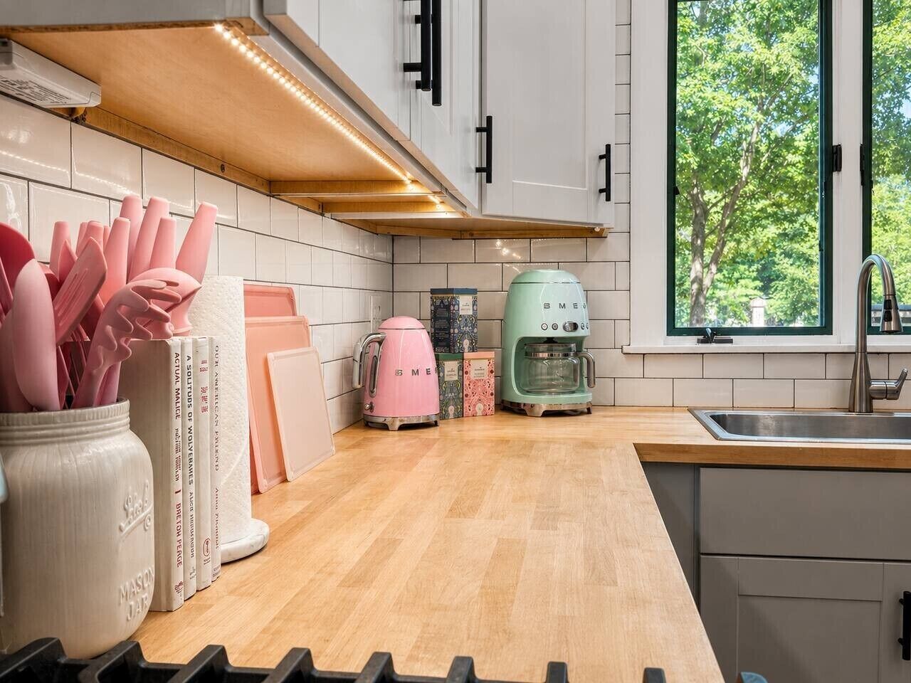 Eine Küche mit weißen Schränken, einer Holzausziehtafel, einem Spülbecken und einem Fenster mit Blick auf Bäume.