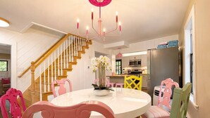 Un espace repas comprenant une table ronde, des chaises, un lustre et un escalier menant à une autre pièce.