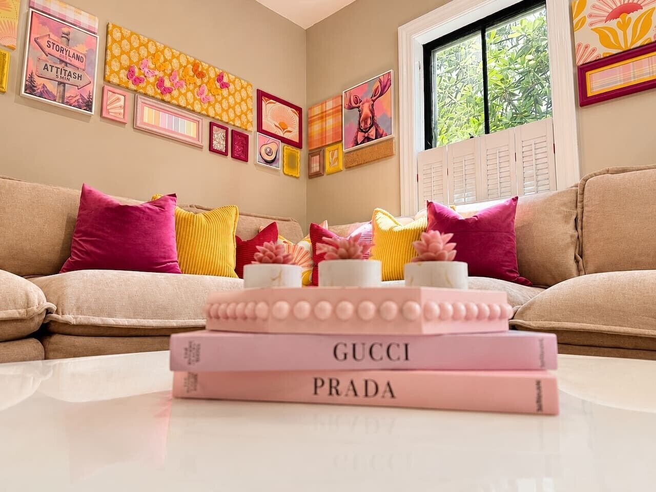 A room with a beige sofa, a coffee table with books, and a window with blinds.