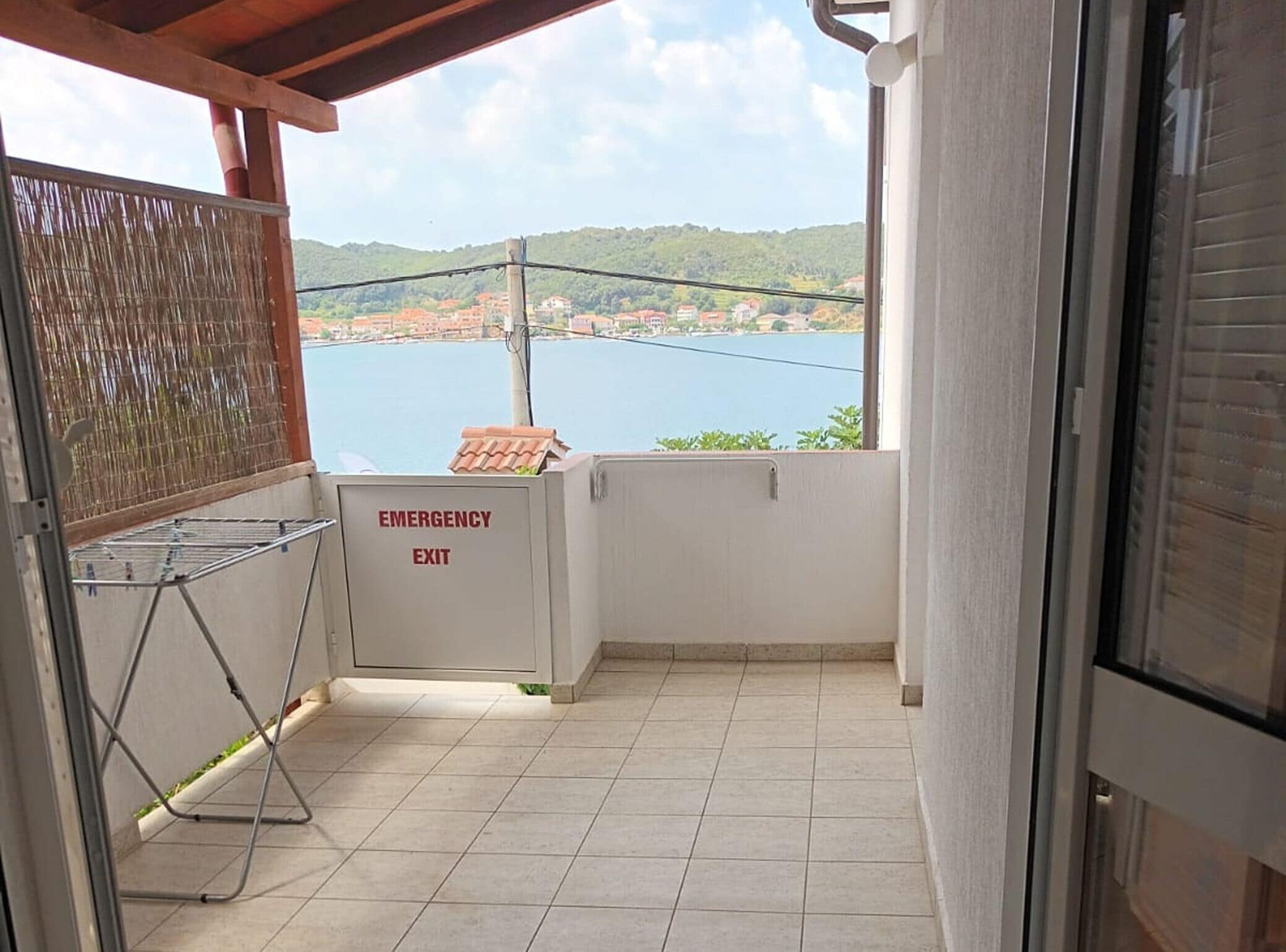 Ein Balkon mit Blick auf einen See und Hügel, ein Notausgangsschild und ein Wäscheständer.