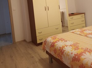 Ein Schlafzimmer mit Holzboden, einem Bett mit Blumenmuster-Bettwäsche, einem zweitürigen Kleiderschrank und einem kleinen Tisch mit Stuhl.