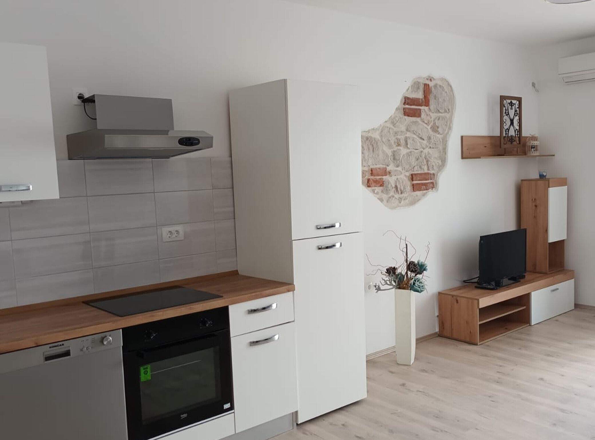 A modern kitchen with a built-in oven, white cabinetry, and a stone accent wall.