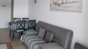 Een woonkamer met een grijze bank, gestreepte kussens, een eettafel met stoelen en een schilderij aan de muur.