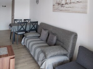 Ein Wohnzimmer mit grauem Sofa, gestreifter Dekokissen, einem Esstisch mit Stühlen und einem Bild an der Wand.
