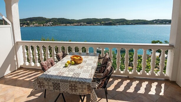 Een balkon met een tafel, stoelen en uitzicht op een meer.
