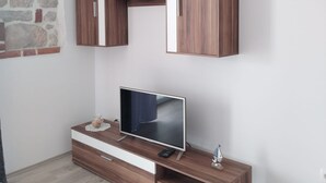 Een moderne woonkamer met een flatscreen televisie op een houten console, een klein decoratief zeilschip, en een stenen muur.