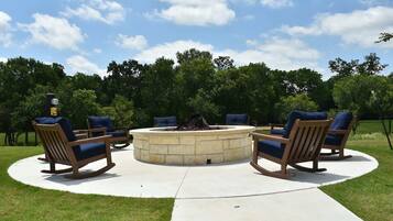 A circular outdoor seating area with stone fire pit and wooden rocking chairs.