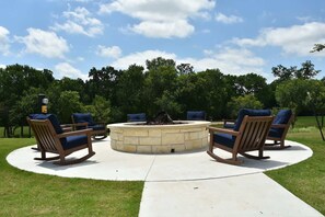 A circular outdoor seating area with stone fire pit and wooden rocking chairs.