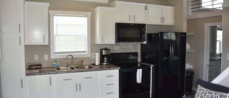 Una cocina moderna con armarios blancos, un refrigerador negro, un microondas y una cafetera.