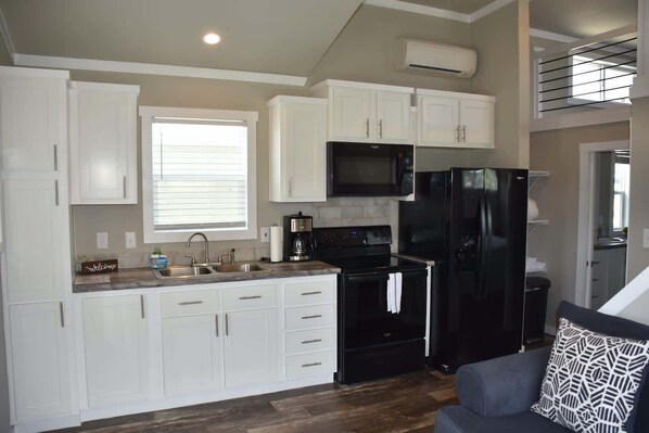 A modern kitchen with white cabinets, a black refrigerator, a microwave, and a coffee maker.