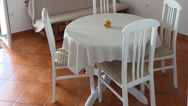 Un'area pranzo con un tavolo rotondo, quattro sedie bianche, una panca e un pavimento piastrellato.