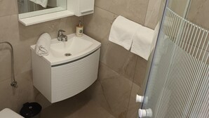 Un bagno con un lavandino bianco, uno specchio sopra, un asciugamano appeso al muro e un box doccia con porta in vetro.
