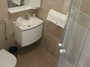 Ein Badezimmer mit einem weißen Waschbecken, einem Spiegel darüber, einem Handtuch an der Wand und einer Duschkabine mit Glastür.