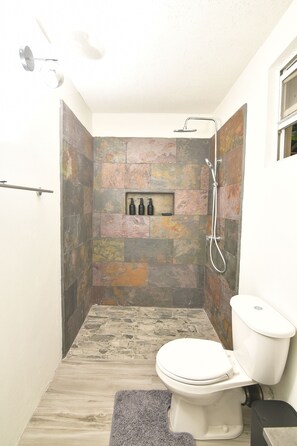 Casa de banho com chuveiro, sanita e um espaço para produtos de higiene pessoal.
