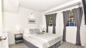 Une chambre à coucher avec un lit, des tables de chevet, une lampe, un tableau au mur et des rideaux.