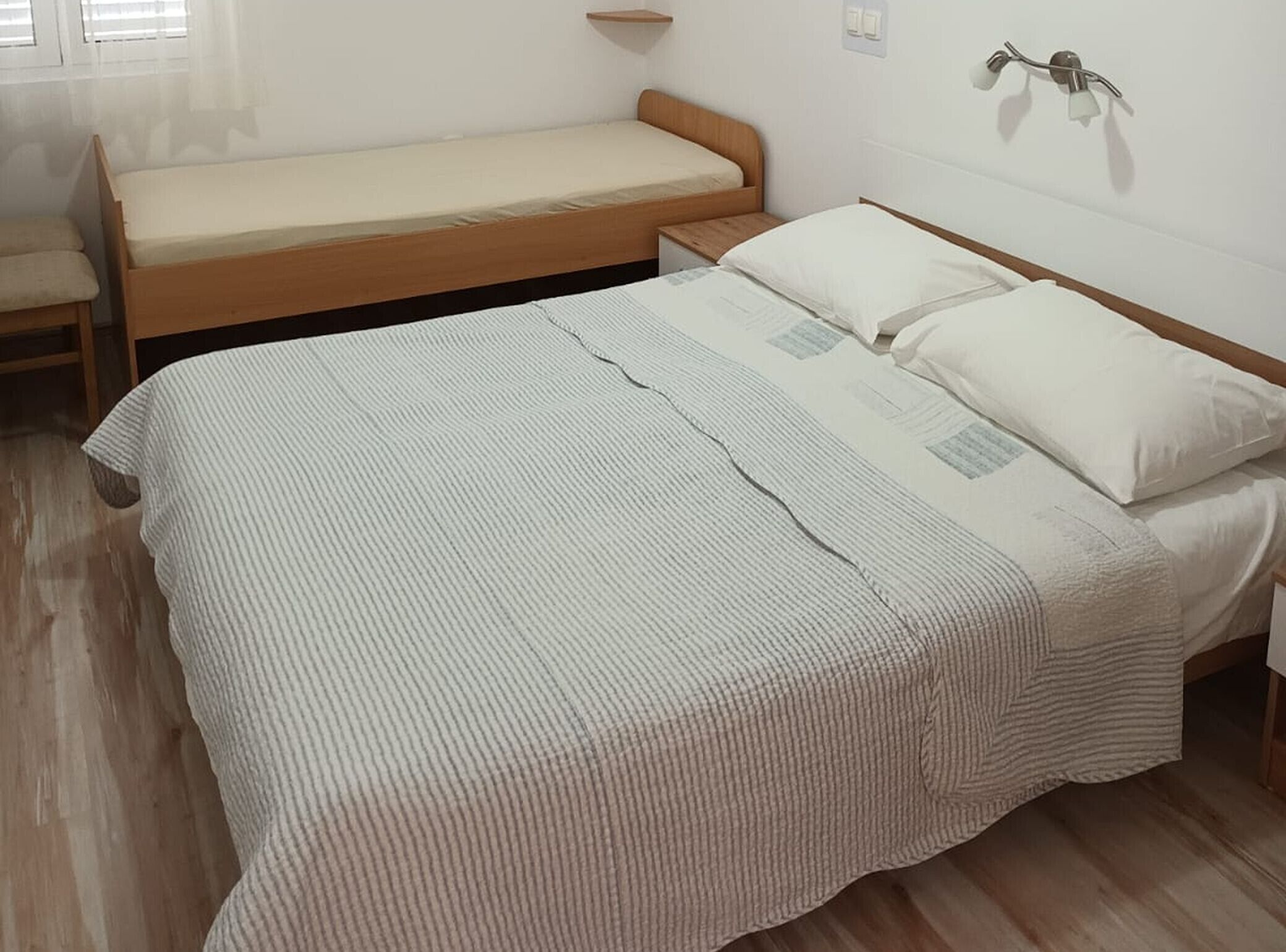 Ein Einzelbett mit gestreifter Bettdecke und Kissen, ein Nachttisch und ein Fenster mit Jalousien.