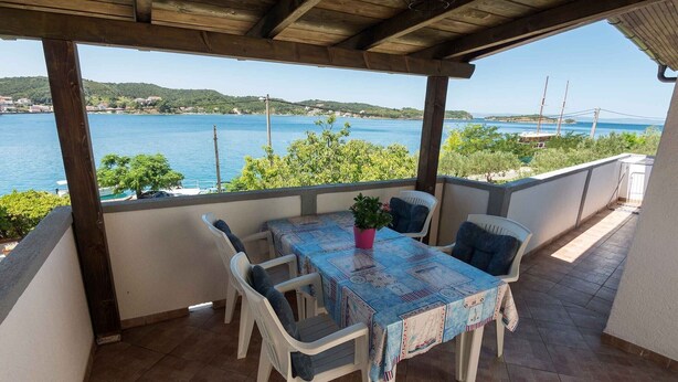 A covered outdoor seating area with a table and chairs, overlooking a body of water and a distant coastline. - Classic One Bedroom Apartment with Sea View and Terrace (Rab)