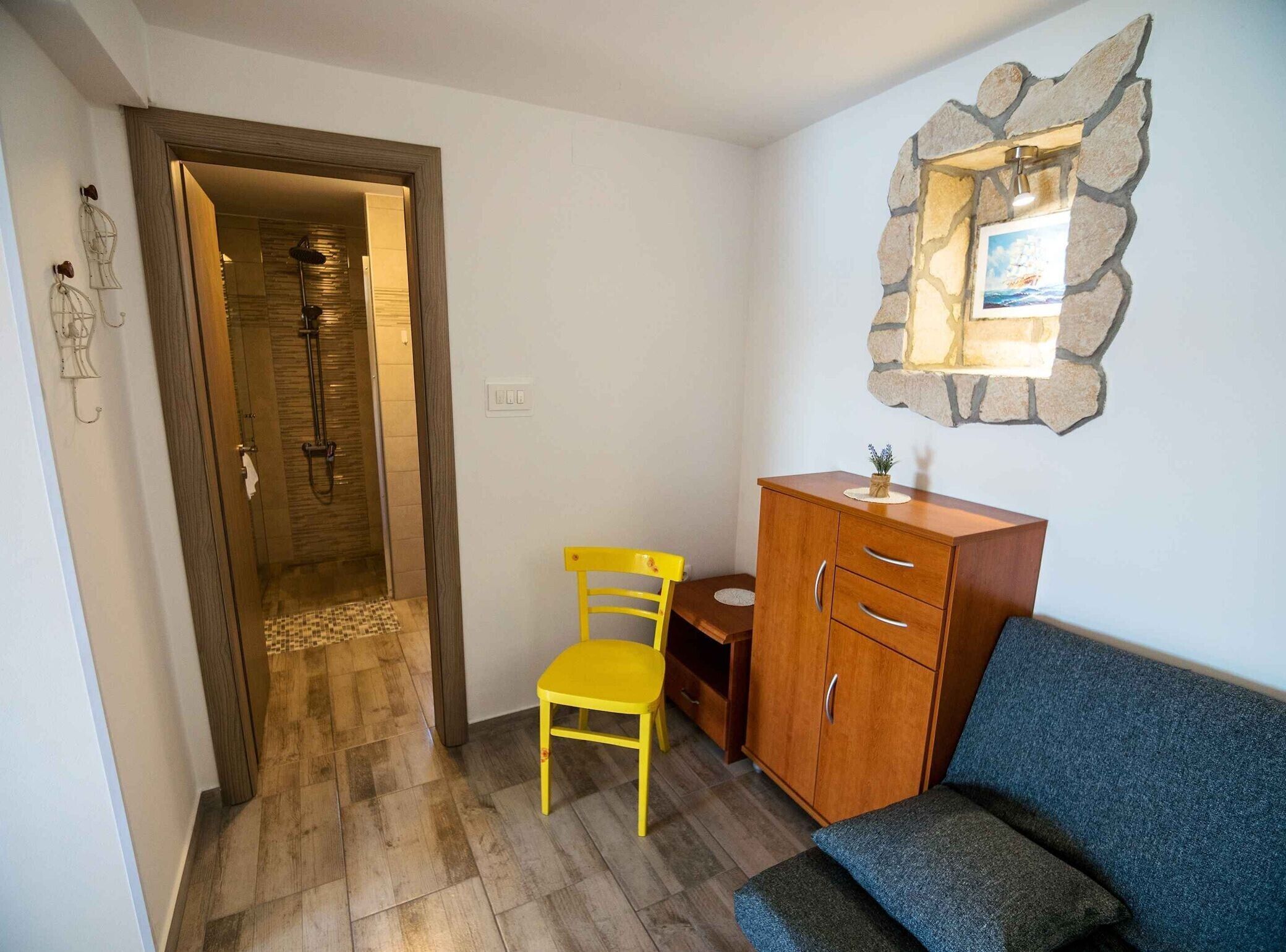 Una habitación con un armario de madera, un sofá azul, una silla amarilla y una zona de ducha.