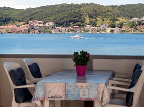 A balcony with a table and chairs, overlooking a body of water with boats and a hillside of buildings. - Classic One Bedroom Apartment with Sea View and Terrace (Rab)