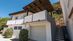 A two-story house with a garage, a covered porch, and a staircase leading to the upper floor. - Classic One Bedroom Apartment with Sea View and Terrace (Rab)