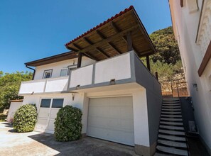 A two-story house with a garage, a covered porch, and a staircase leading to the upper floor. - Classic One Bedroom Apartment with Sea View and Terrace (Rab)