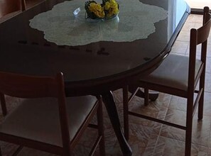 A round table with a glass top, surrounded by four wooden chairs with cushioned seats. - Two Bedroom Apartment with Sea View and Terrace (Rogoznica)