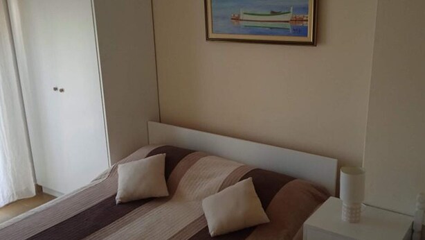 A hotel room with a bed, pillows, a nightstand, and a painting of a boat on the wall. - Classic One Bedroom Apartment with Sea View and Balcony (Rogoznica)