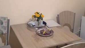 A dining table with a vase of yellow flowers, a bowl of fruit, and a plate with a drink. - Classic One Bedroom Apartment with Sea View and Balcony (Rogoznica)