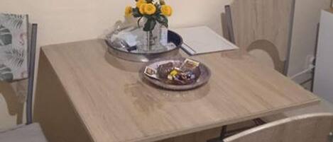A dining table with a vase of yellow flowers, a bowl of fruit, and a plate with a drink.