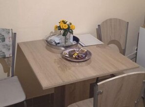 A dining table with a vase of yellow flowers, a bowl of fruit, and a plate with a drink. - Classic One Bedroom Apartment with Sea View and Balcony (Rogoznica)