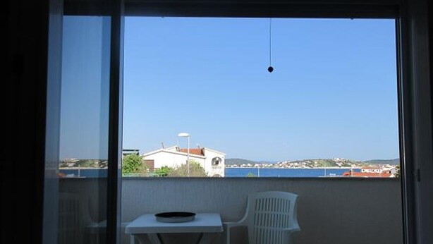 Un balcón con mesa y sillas, con vista a una zona costera con edificios y cielo despejado.