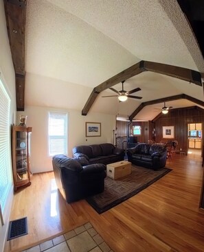 A spacious living area with a high ceiling, wooden beams, a ceiling fan, and a fireplace. - Old Town Walkable Windsor (Windsor)
