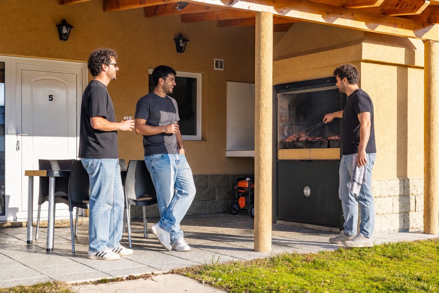 An outdoor patio area with a barbecue grill, a seating arrangement, and a building entrance.