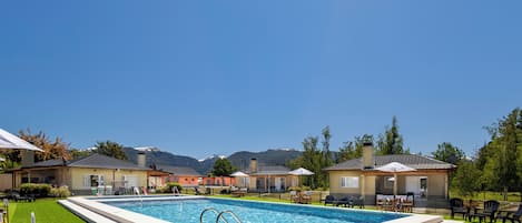 A swimming pool with a view of mountains in the background, surrounded by houses with outdoor seating.