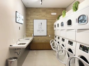 A laundry room with multiple washing machines, a sink, and a wooden wall. - The Collection Perdizes (São Paulo)