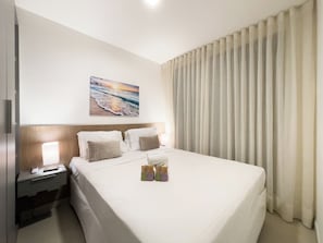 A hotel room with a bed, bedside table, lamp, and a painting on the wall.