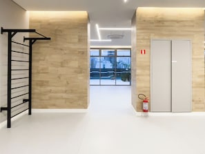 A hallway with a black metal rack, a fire extinguisher, and a double door. - The Collection Perdizes (São Paulo)