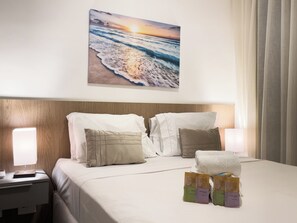 A hotel room with a bed, pillows, a nightstand, a lamp, and a painting of a beach scene. - The Collection Perdizes (São Paulo)