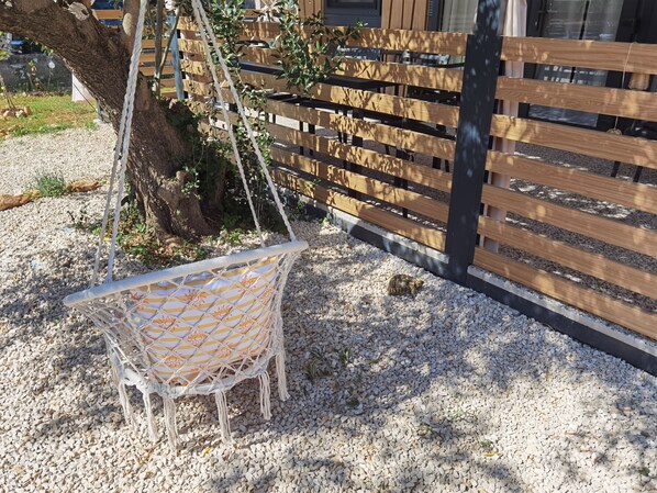 En hängstol med ett mönstrat sittdyn, ett trästaket och ett träd i ett område med grus.