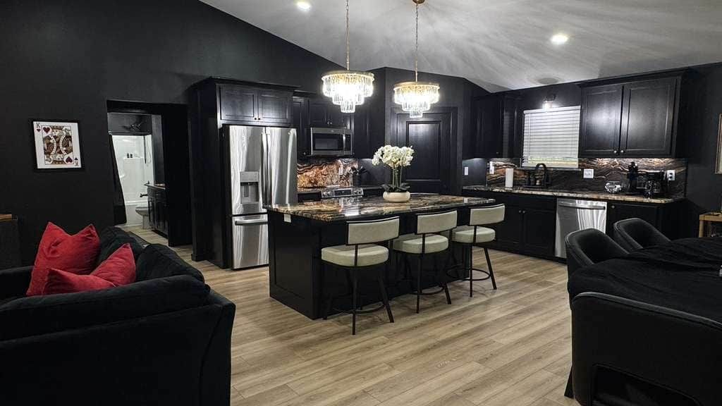 A modern kitchen with a central island, bar stools, and a chandelier.