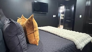 A bedroom with a bed, a TV mounted on the wall, and a door leading to another room. - Casino Royale near WinStar - King Suite (Thackerville)
